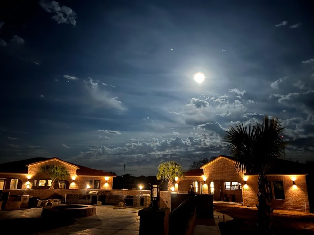 a building with lights on and palm trees and a cloudy sky